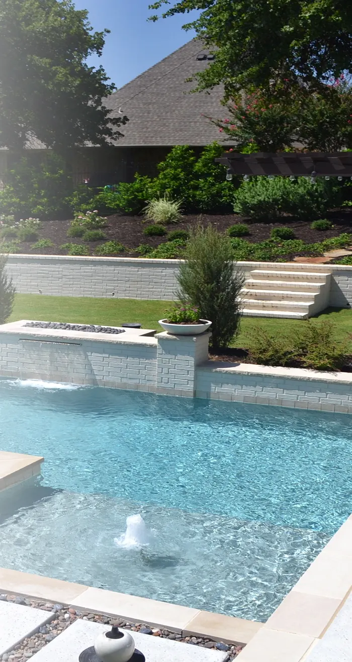 A pool with deck bubblers in front of a raised stone planter wall