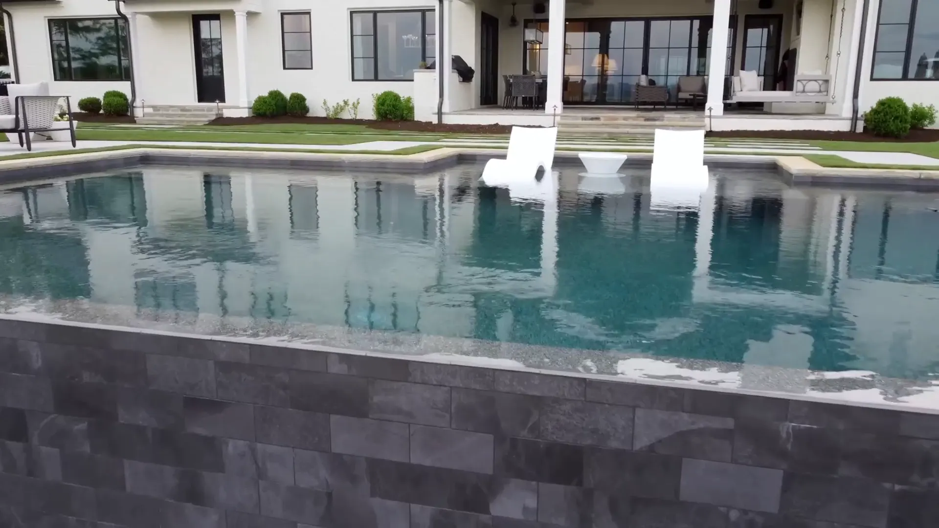 A vanishing-edge pool spilling over a stacked stone wall at dusk